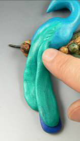 Blue and green clay being pressed onto peacock